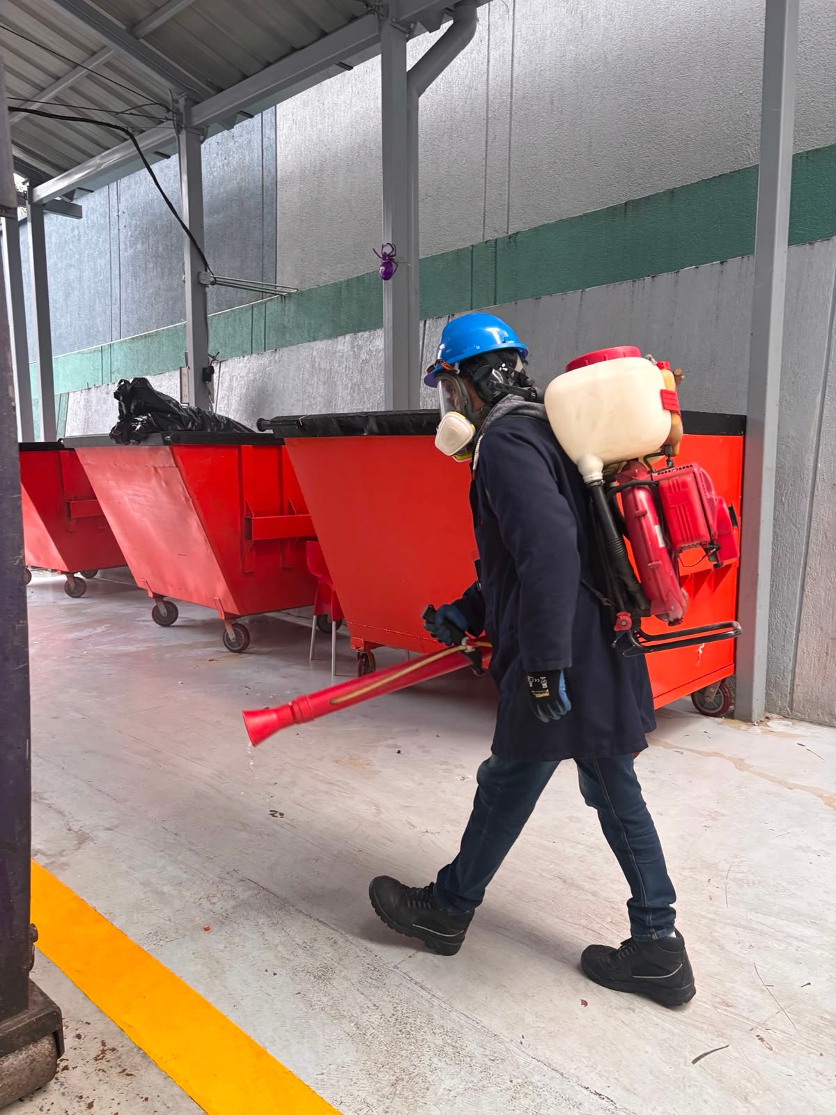 Técnico aplicando control de plagas junto a contenedores industriales